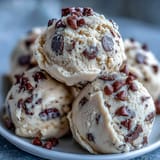 A hand holding a scoop of Greek Yogurt Cookie Dough with a bite taken out, revealing a rich, buttery texture.