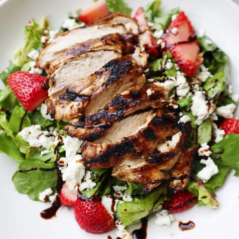 Juicy grilled chicken slices atop mixed greens with strawberries, red onion, and crumbled goat cheese, drizzled with honey balsamic glaze.