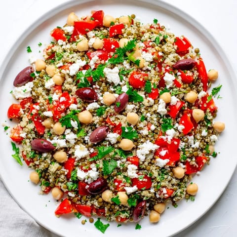 A vibrant Greek Power Salad with lentils, quinoa, chickpeas, and fresh veggies drizzled in zesty vinaigrette.
