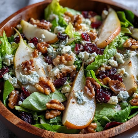 A close-up view of a vibrant Pear Gorgonzola Salad featuring juicy sliced pears, crumbled blue cheese, and toasted walnuts on fresh greens, drizzled with honey-balsamic vinaigrette.