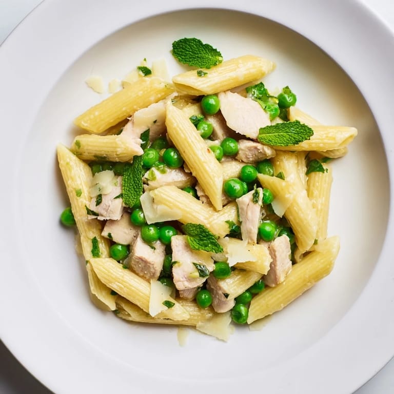 Close-up of Pea & Mint Chicken Pasta reveals al dente penne, juicy chicken pieces, and vibrant peas tossed with fresh herbs.